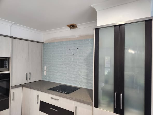 Grey-blue brick splashback in corner of dark cabinetry kitchen