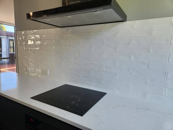 White glossy subway under stainless rangehood with marble bench
