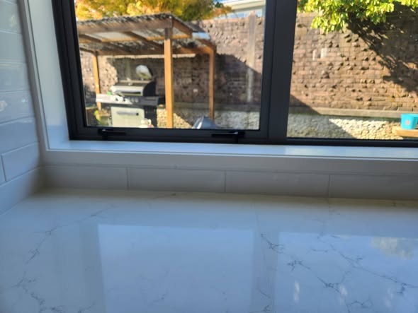 White glossy splashback meeting windowsill with marble bench and autumn maple view
